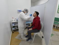 Медицинский сотрудник Гемотеста в защитной экипировке берет образец слюны у мужчины в центре тестирования на COVID-19 в Москве. Фото: AFP